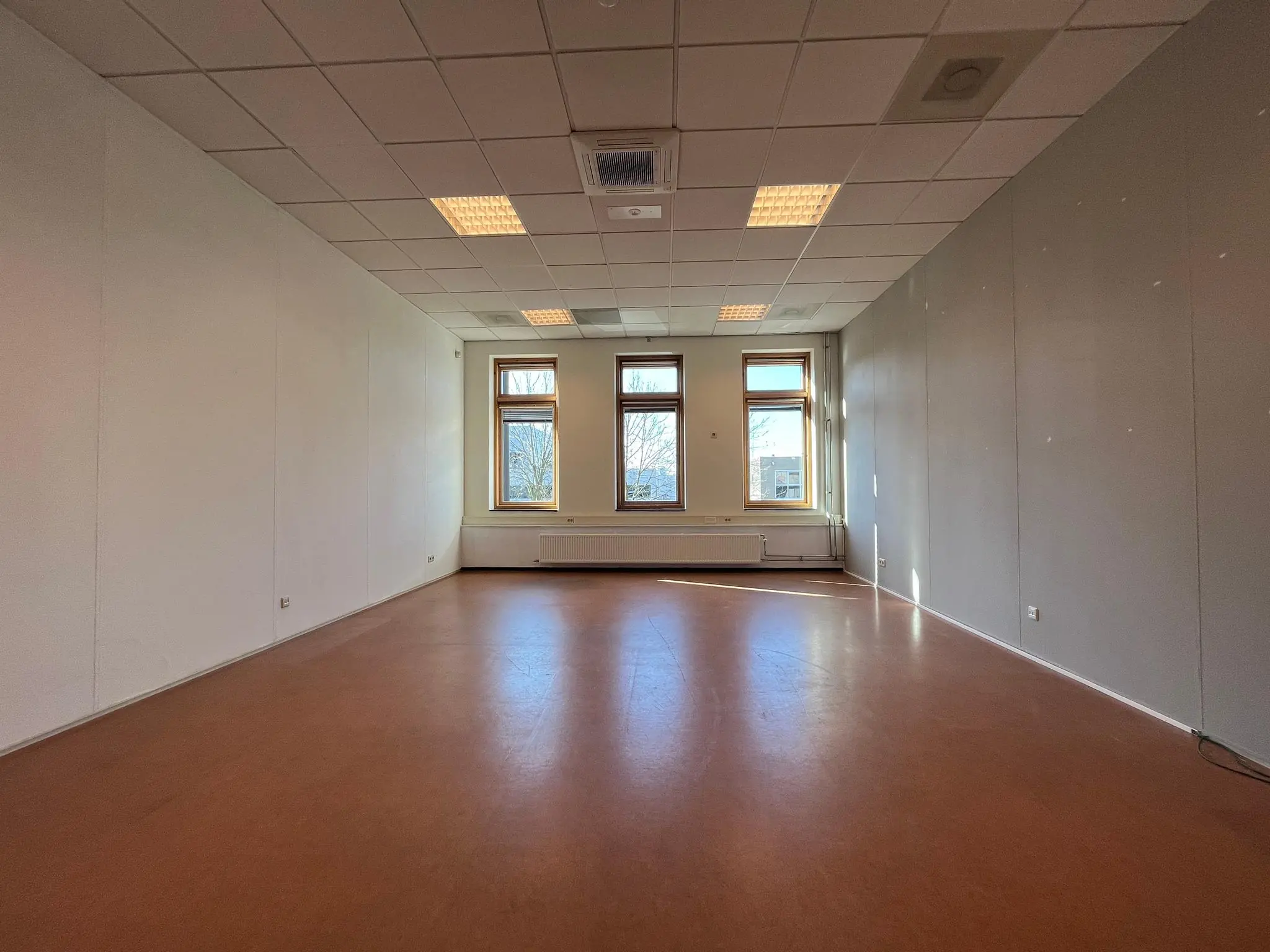 Leeg klaslokaal in Gebouw Veldzigt met drie grote ramen en systeemplafond.
