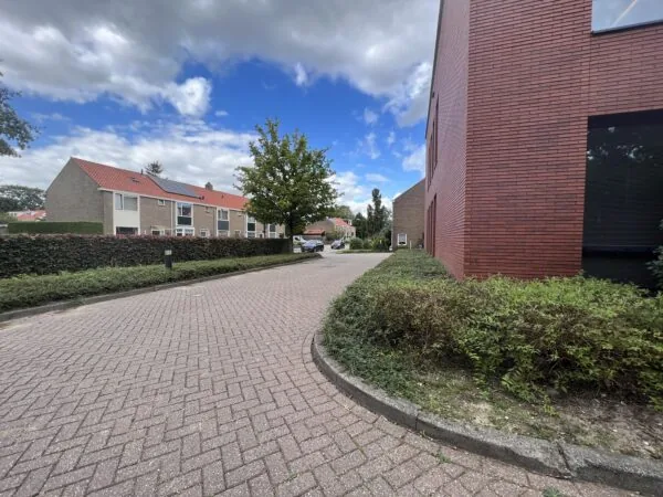 Een rustige straat met huizen, omgeven door heggen en bomen onder een deels bewolkte lucht.