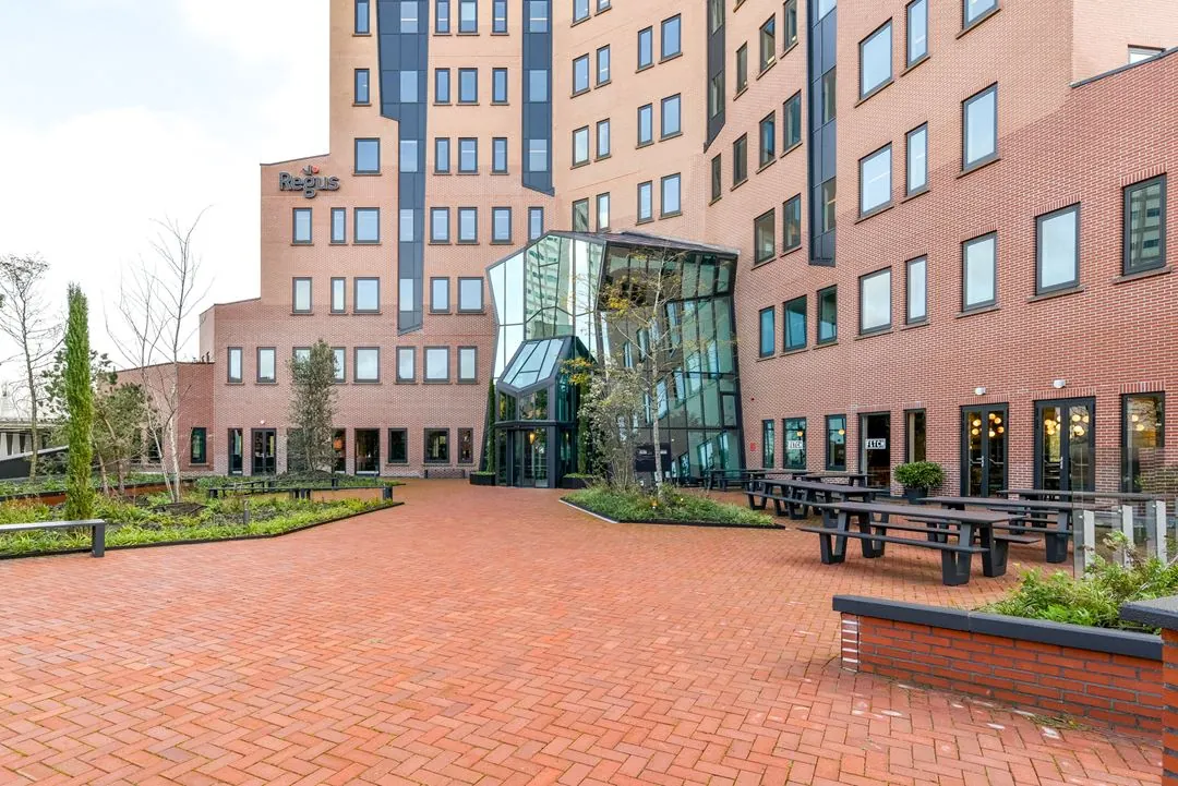 Buitenzijde van het Regus-kantoor aan de Kingsfordweg met bakstenen gevel, glazen entree en omliggend terras met zitbanken.