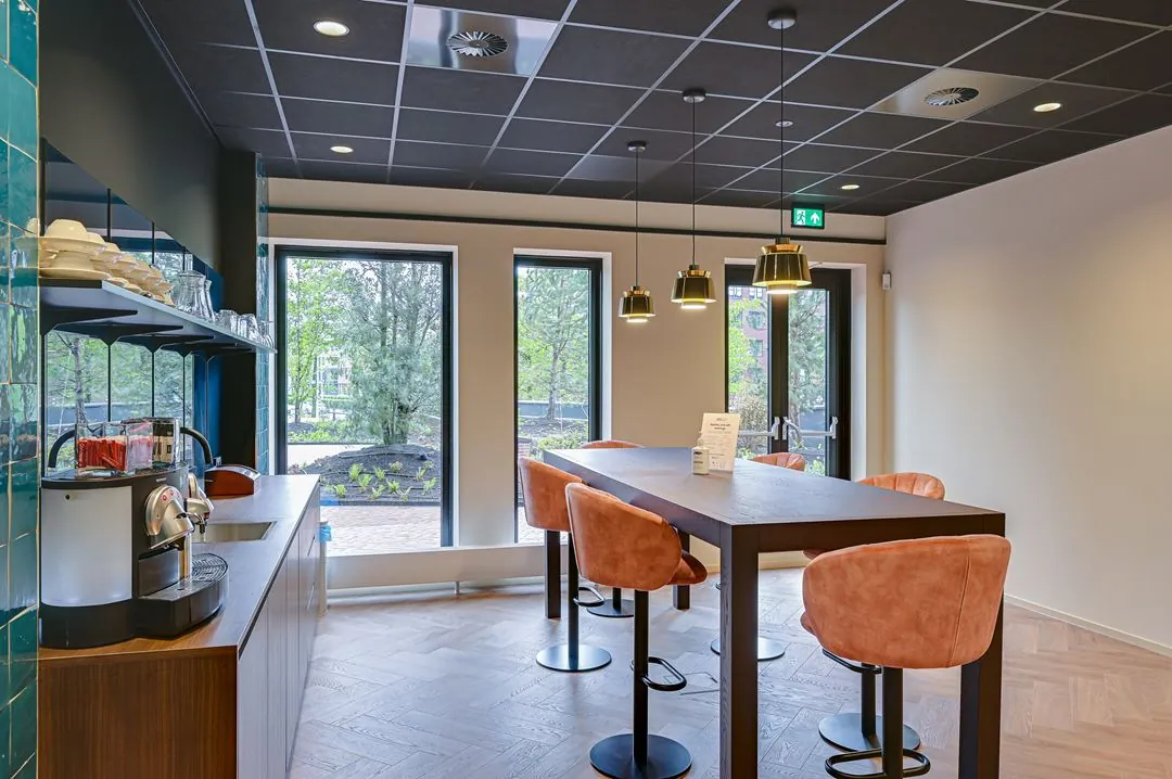 Moderne koffieruimte aan de Kingsfordweg met hoge tafel, fluwelen barkrukken en uitzicht op een groene buitenruimte.
