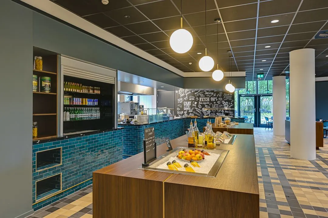 Modern ingerichte bedrijfskantine aan de Kingsfordweg met een selfservice-eiland vol fruit, sapjes en olijfolie.