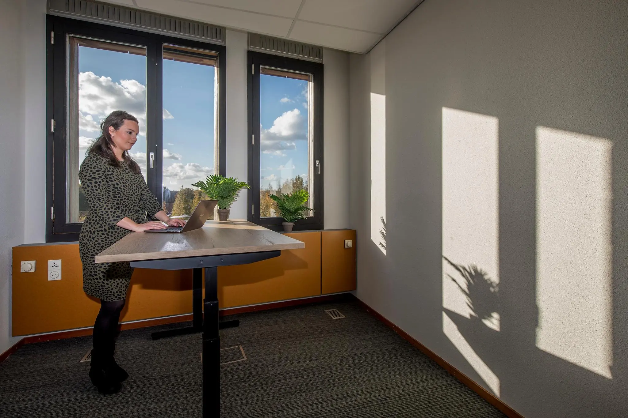 Vrouw werkt staand achter een bureau met laptop in een zonovergoten kantoor aan de Fokkerstraat.