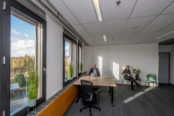 Twee mensen in een modern en licht kantoor aan de Fokkerstraat met grote ramen en uitzicht op een herfstig landschap.