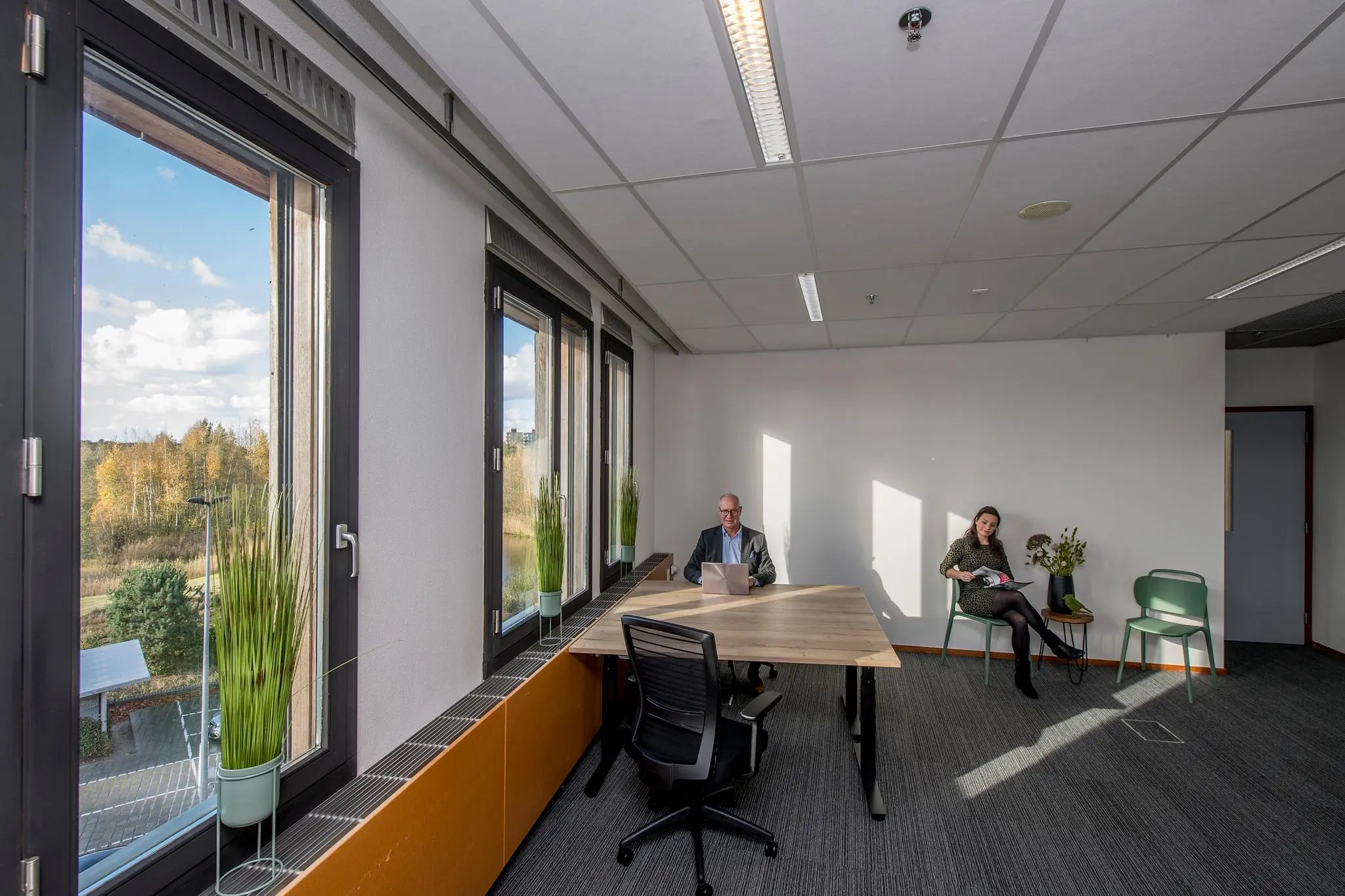 Twee mensen in een modern en licht kantoor aan de Fokkerstraat met grote ramen en uitzicht op een herfstig landschap.