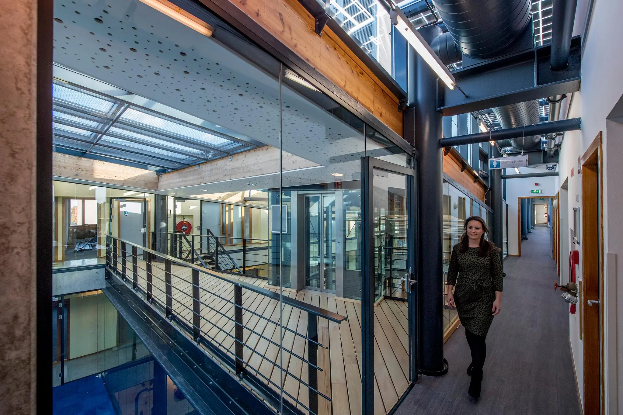 Vrouw loopt door een modern kantoorgebouw aan de Fokkerstraat met glazen wanden en zichtbare houten en stalen constructie.