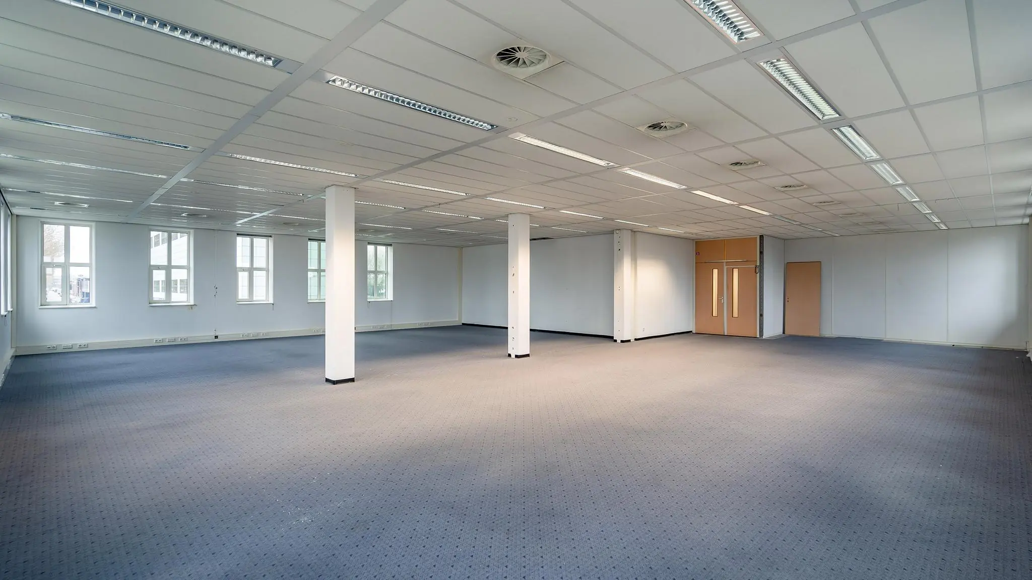 Leeg kantoorpand aan de Vareseweg met systeemplafond, tapijtvloer en grote ramen.