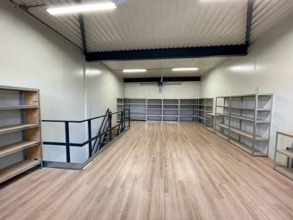 Ruimte met houten vloer, metalen stellingkasten en een trap, gelegen aan de Aalsmeerderweg.