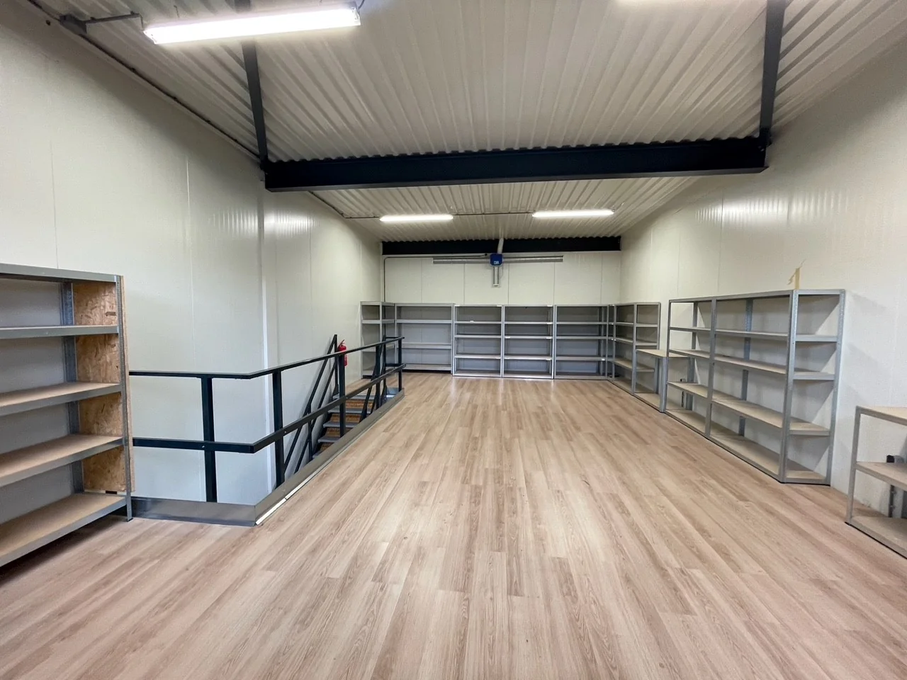 Ruimte met houten vloer, metalen stellingkasten en een trap, gelegen aan de Aalsmeerderweg.