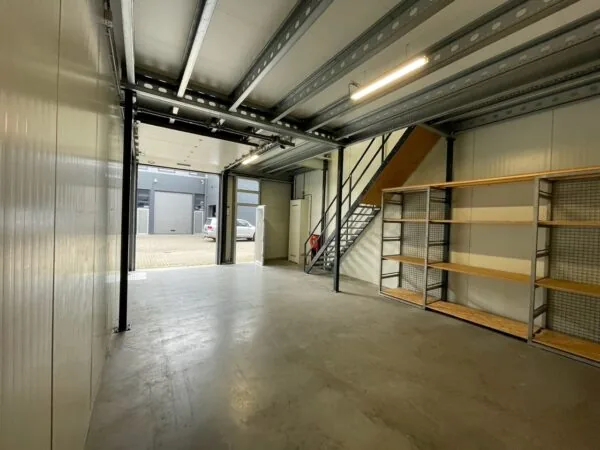 Interieur van een opslag- of bedrijfsruimte aan de Aalsmeerderweg met metalen trap, houten stellingen en een open garagedeur naar buiten.