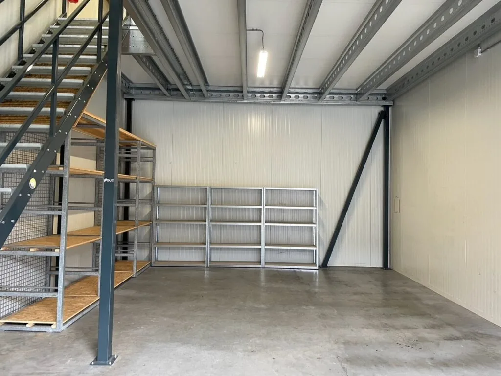 Opslagruimte aan de Aalsmeerderweg met metalen stellingen, betonnen vloer en stalen trap naar een verhoogd platform.