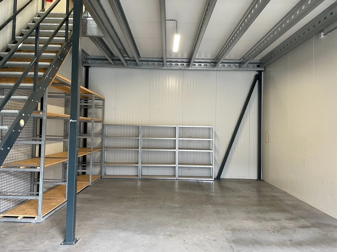 Opslagruimte aan de Aalsmeerderweg met metalen stellingen, betonnen vloer en stalen trap naar een verhoogd platform.