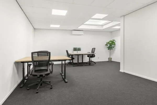 Moderne, minimalistische kantoorruimte aan de Nijverheidsweg met bureaus, bureaustoelen en een kunstplant.