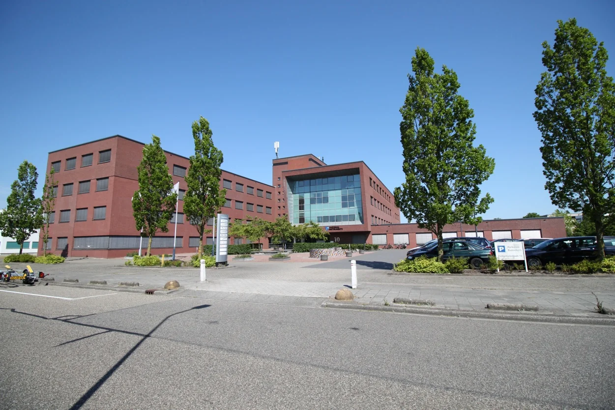 Zakelijk kantoorgebouw aan de Pompmolenlaan met bakstenen gevel en grote ramen, omgeven door bomen en parkeerplaatsen.