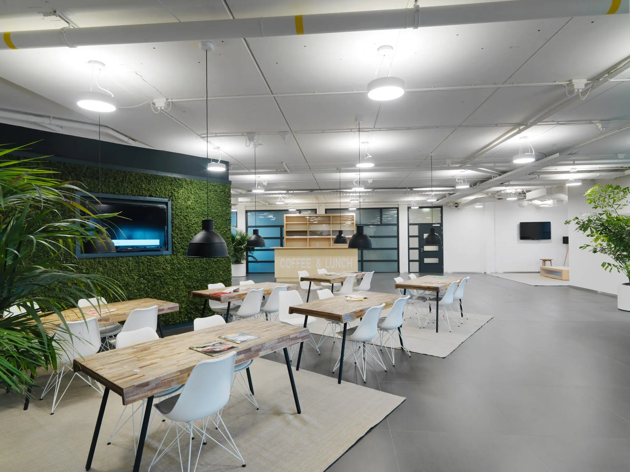Moderne, open bedrijfsruimte aan de Pompmolenlaan met houten tafels, witte stoelen, groene planten en een koffiehoek.