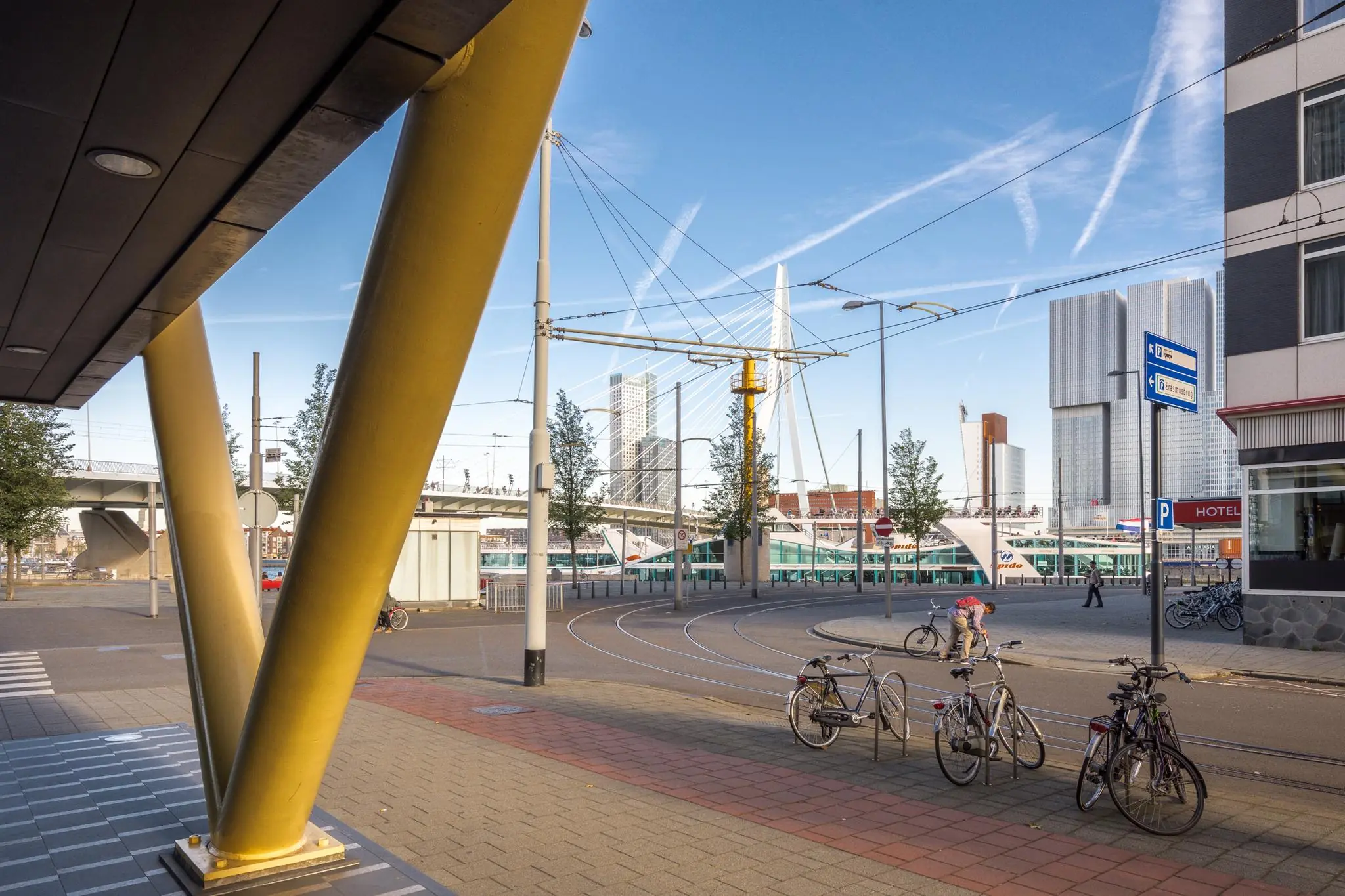 Straatbeeld van de Westerstraat in Rotterdam met zicht op de Erasmusbrug, fietspad, geparkeerde fietsen en moderne hoogbouw.