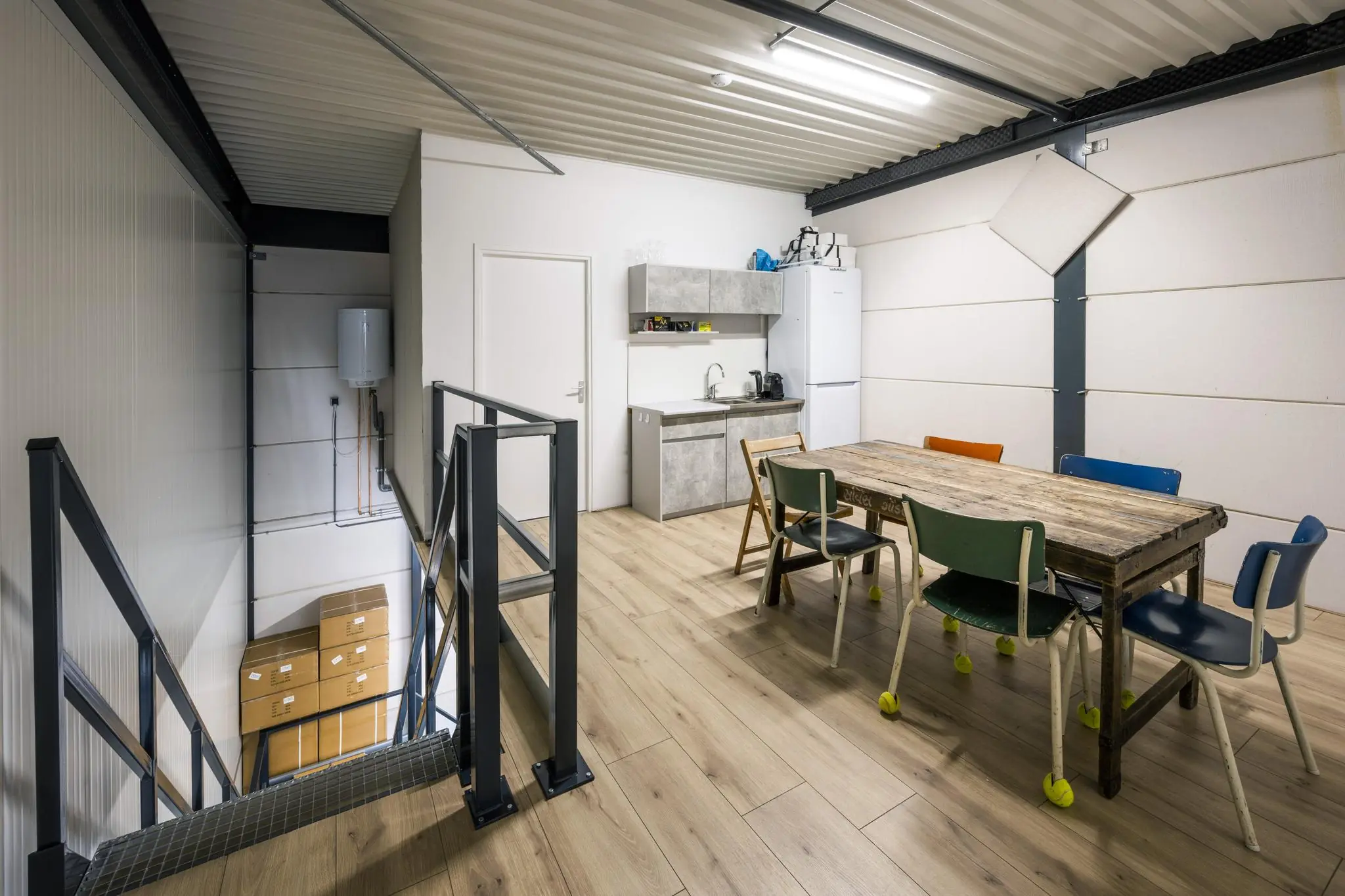 Bovenverdieping van een bedrijfsruimte aan de Aalsmeerderweg met een kantine met houten tafel, kleurige stoelen en kitchenette.
