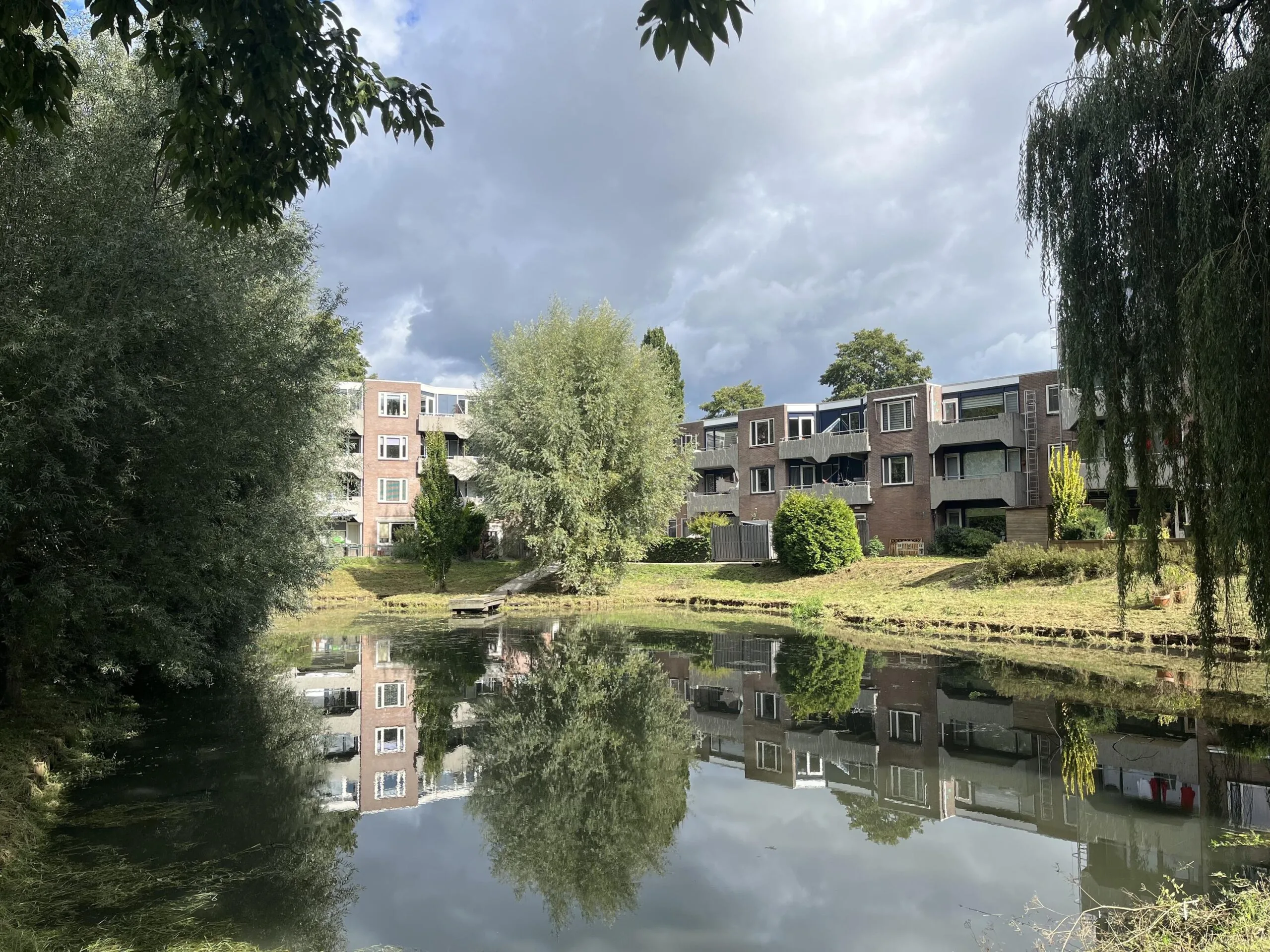 Appartementencomplex aan het water met bomen weerspiegeld in het water op een bewolkte dag.