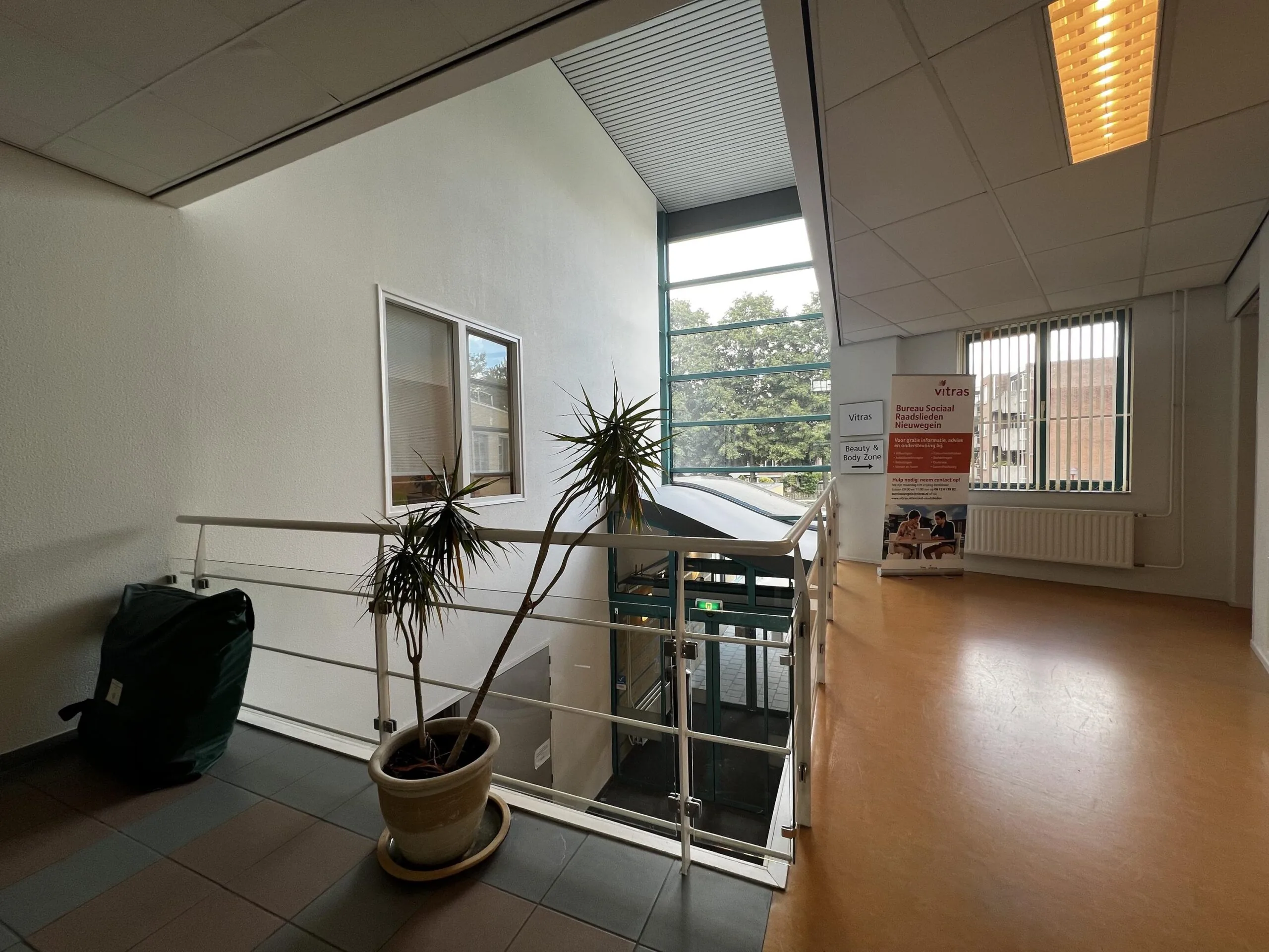 Een lichte overloop met een plant, zicht naar buiten en een bord van Bureau Sociaal Raadslieden Nieuwegein.