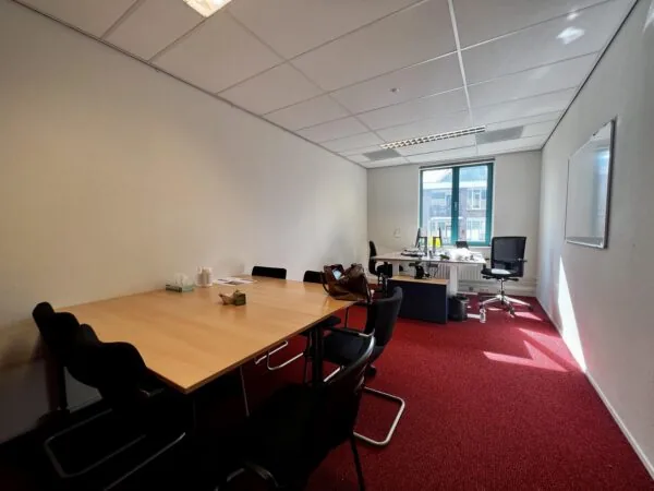 Een vergaderruimte met een houten tafel, zwarte stoelen en een bureau bij het raam.