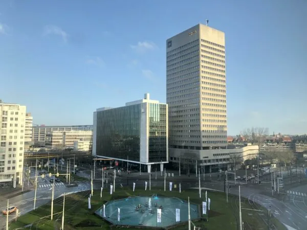 Zicht op het Hofplein in Rotterdam met fontein, omringende kantoorgebouwen en tramlijnen op een zonnige dag.