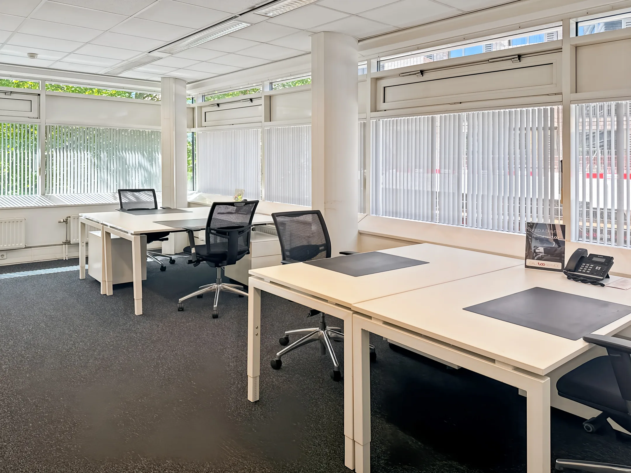 Licht en modern kantoorinterieur met meerdere bureaus en stoelen bij grote ramen.