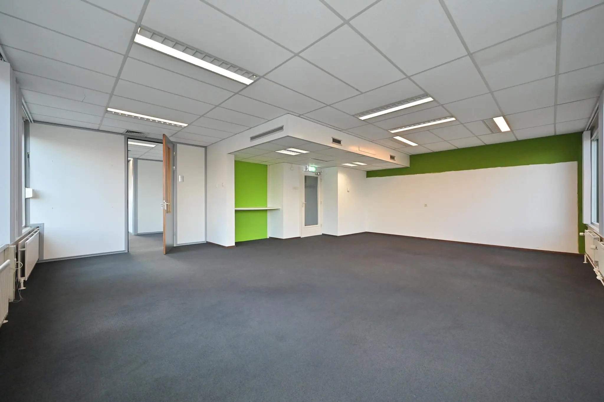 Leeg kantoorpand aan de Bezuidenhoutseweg met wit-groene muren, systeemplafond en grijs tapijt.