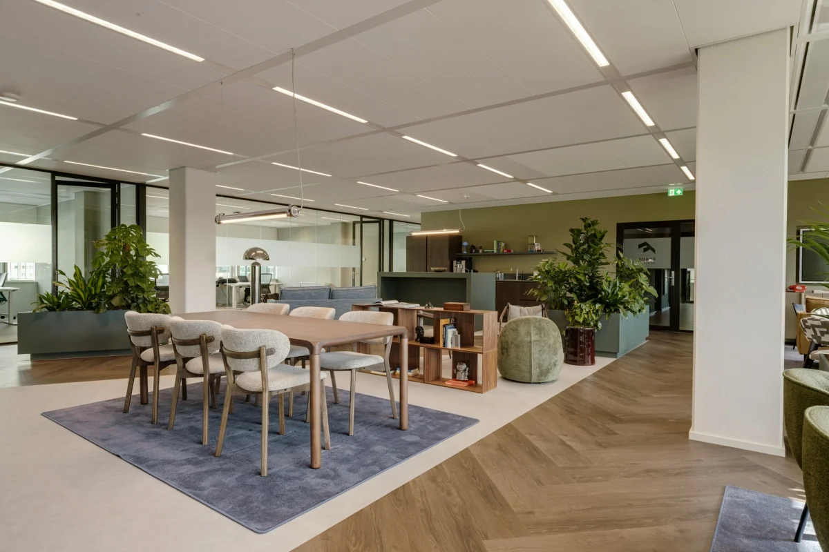Moderne kantoorruimte met een houten tafel en comfortabele stoelen, omringd door groene planten en glazen wanden.