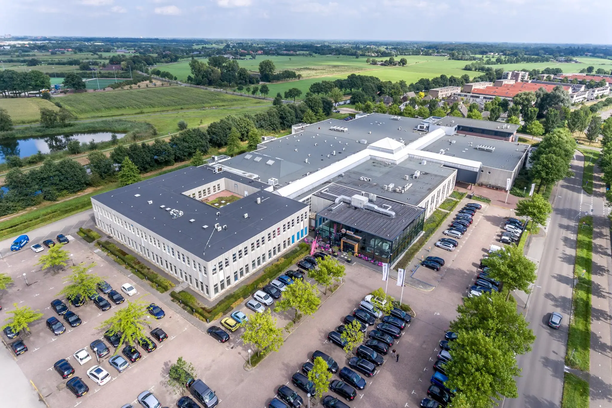 Luchtfoto van een groot kantoorgebouw aan de Plesmanstraat met omliggende parkeerplaatsen en groen landschap.