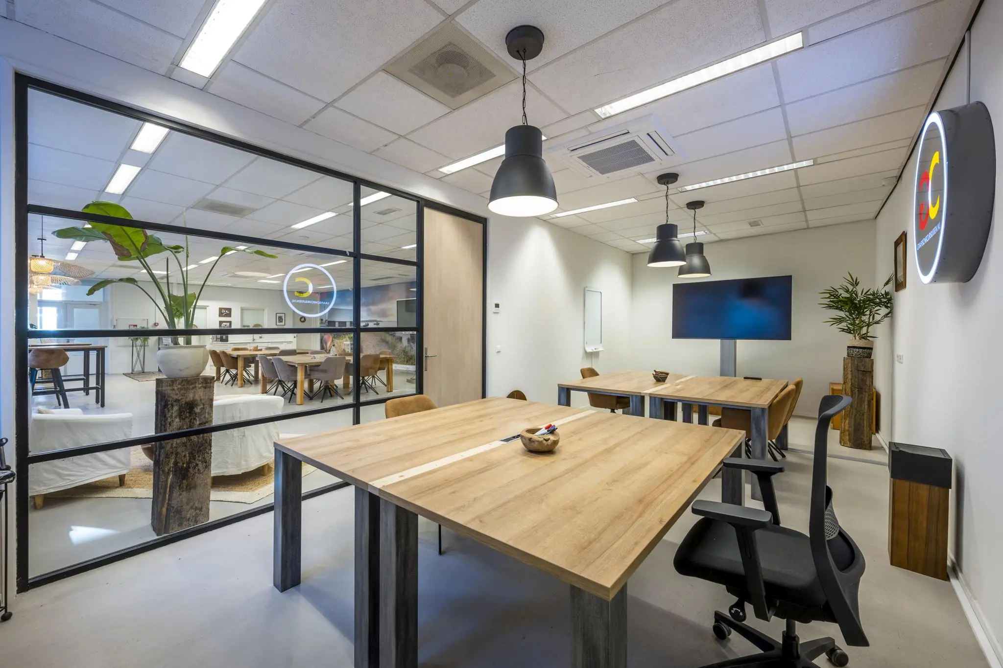 Moderne vergaderruimte in Helicopterstraat-kantoor met houten tafels, designstoelen en glazen wand naar een open kantoorruimte.