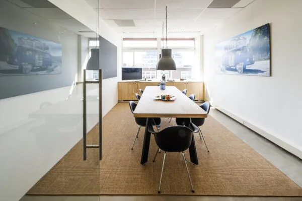 Moderne vergaderruimte aan de Helicopterstraat met een lange houten tafel, zwarte stoelen en grote wandfoto's van een busje.
