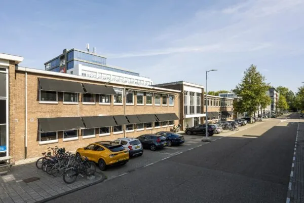 Kantoorpanden aan de Vliegtuigstraat in Amsterdam met geparkeerde auto's en fietsen op een zonnige dag.