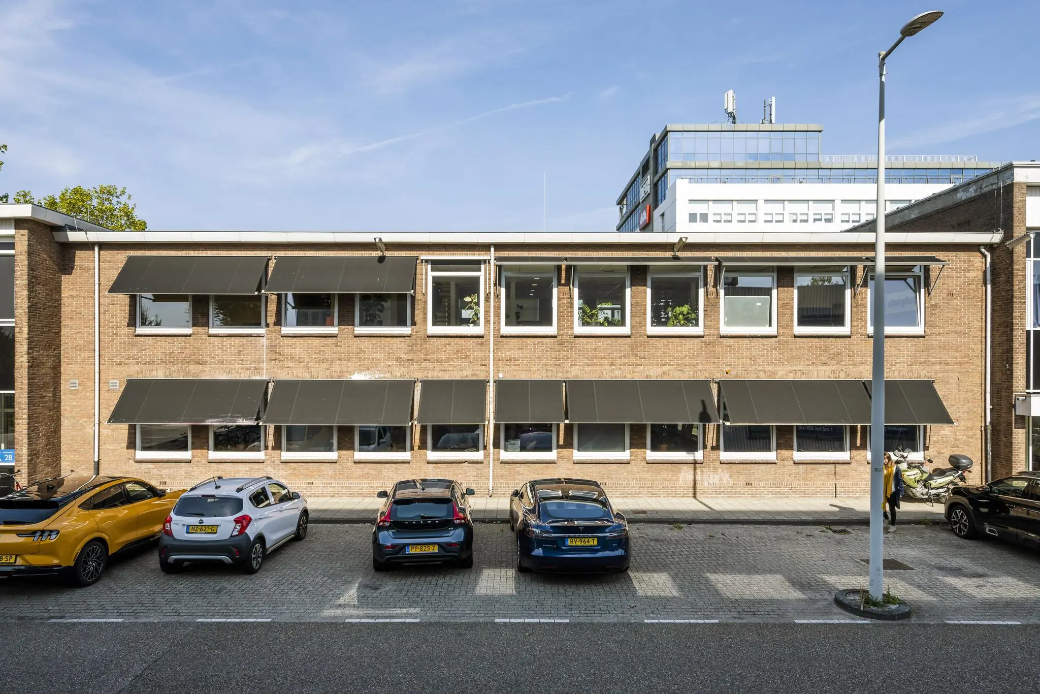 Vooraanzicht van een bakstenen kantoorgebouw aan de Vliegtuigstraat met geparkeerde auto's ervoor.