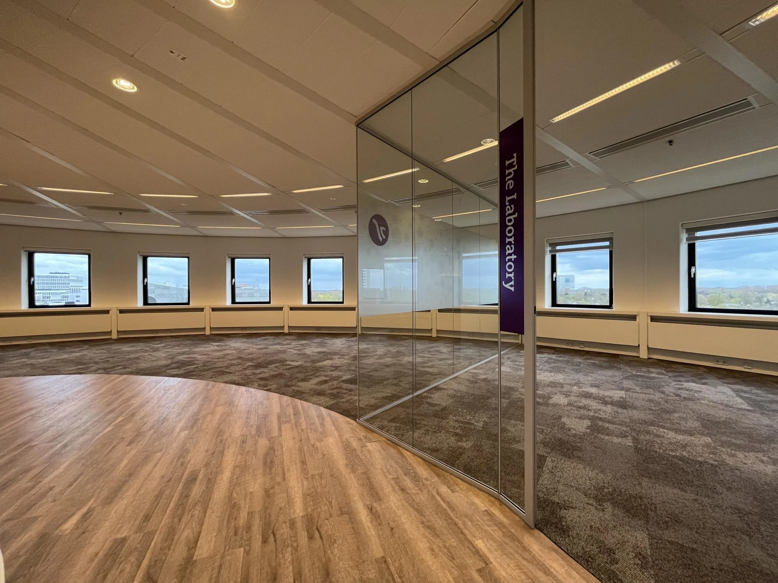 Een moderne, lege kantoorruimte met ramen en een glazen wand gemarkeerd als "The laboratory" te Euclideslaan.