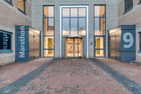 Ingang van kantoorgebouw Marathon 9 met automatische draaideur en moderne gevel.