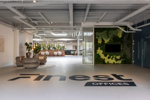 Een moderne kantoorruimte met planten, zitgedeelte en muurdecoratie met het logo "Finest Offices" op de vloer.