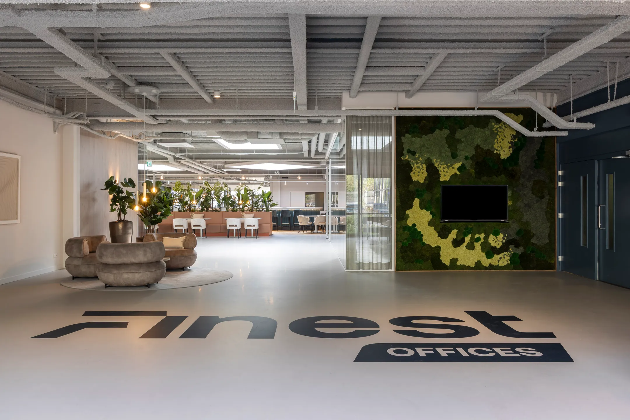 Een moderne kantoorruimte met planten, zitgedeelte en muurdecoratie met het logo "Finest Offices" op de vloer.