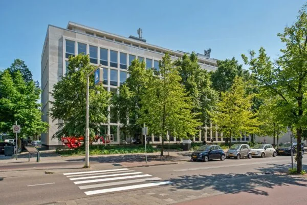 Kantoorgebouw aan de Bezuidenhoutseweg in Den Haag met bomen en geparkeerde auto's op de voorgrond.