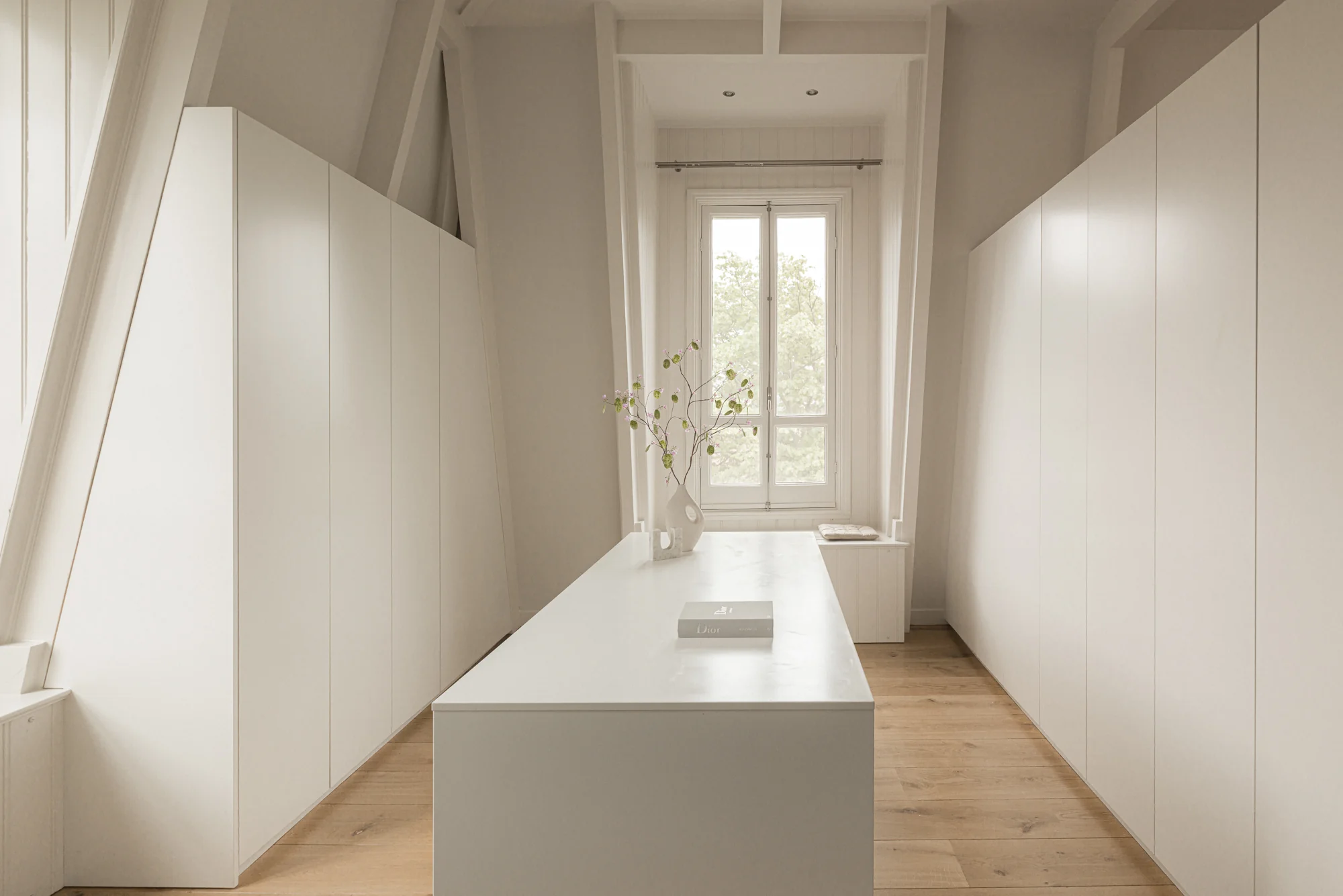 Minimalistisch, licht interieur van een moderne inloopkast aan de Weteringschans met witte kasten, houten vloer en een centraal eiland.