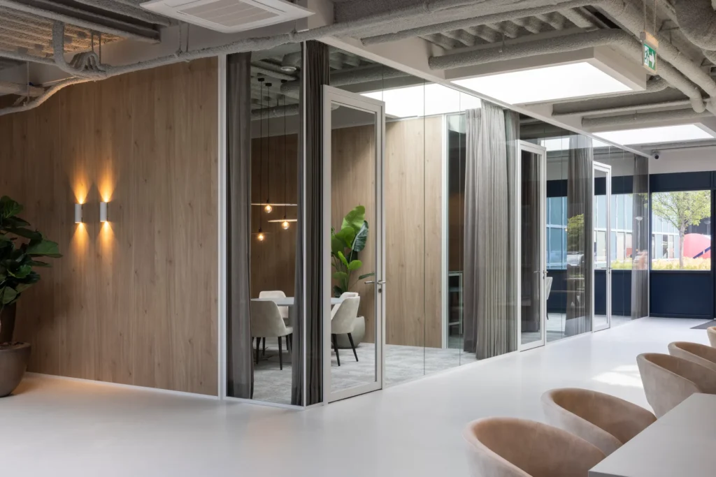 Een moderne kantoorruimte met glazen wanden, een vergadertafel en stoelen, en een grote plant.