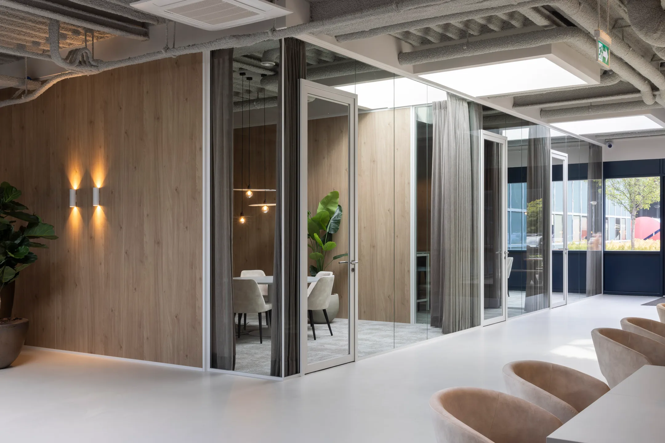 Een moderne kantoorruimte met glazen wanden, een vergadertafel en stoelen, en een grote plant.