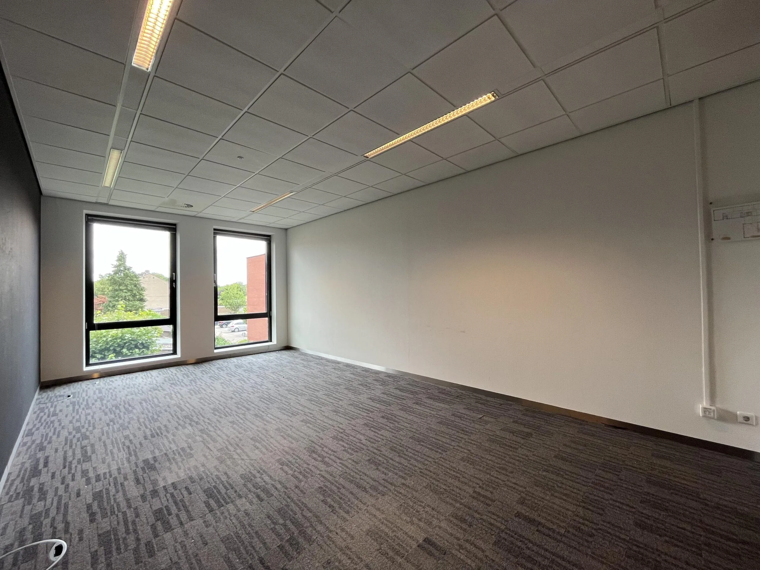 Leeg kantoor met donkere vloerbedekking en grote ramen aan de Groenekanseweg.