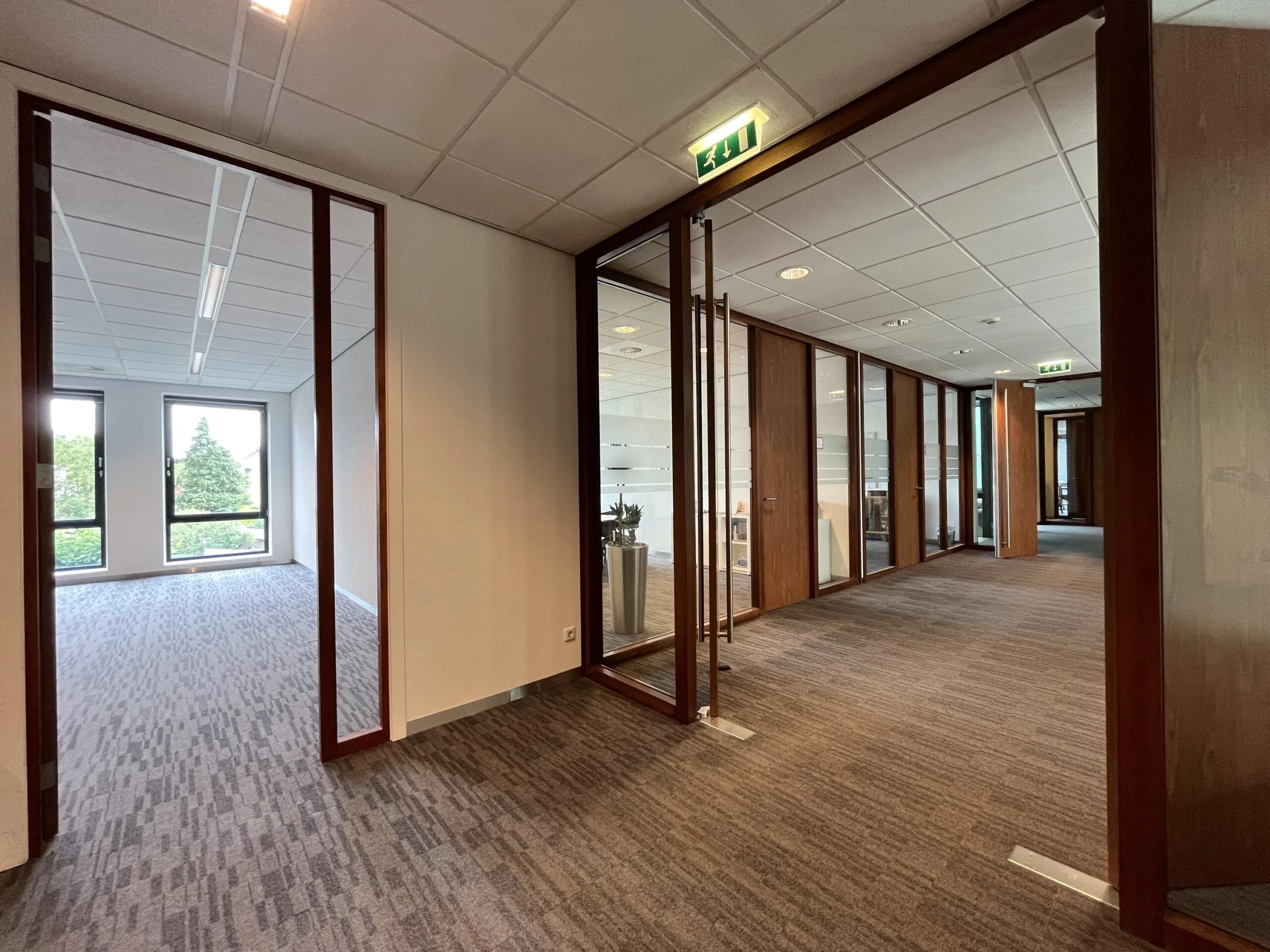 Een modern kantoorinterieur met glazen wanden, tapijten vloeren en ramen met uitzicht op groen aan de Groenekanseweg.