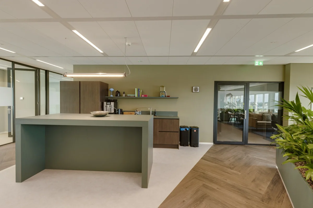 Moderne kantoorruimte met een keukenblok, groene muur, en planten.