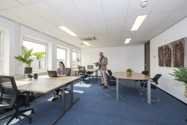 Licht en modern kantoor met een vrouw werkend aan een laptop en een man die een tijdschrift leest.