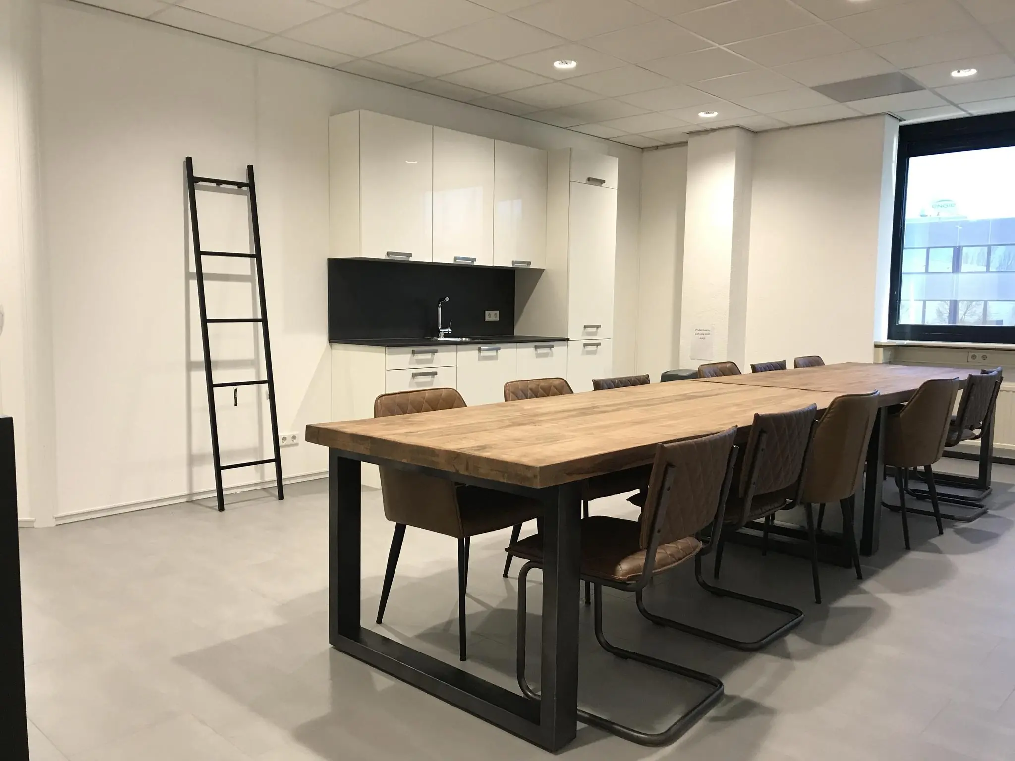 Moderne vergaderruimte aan de Cypresbaan met lange houten tafel, keukenblok en metalen ladder tegen de muur.