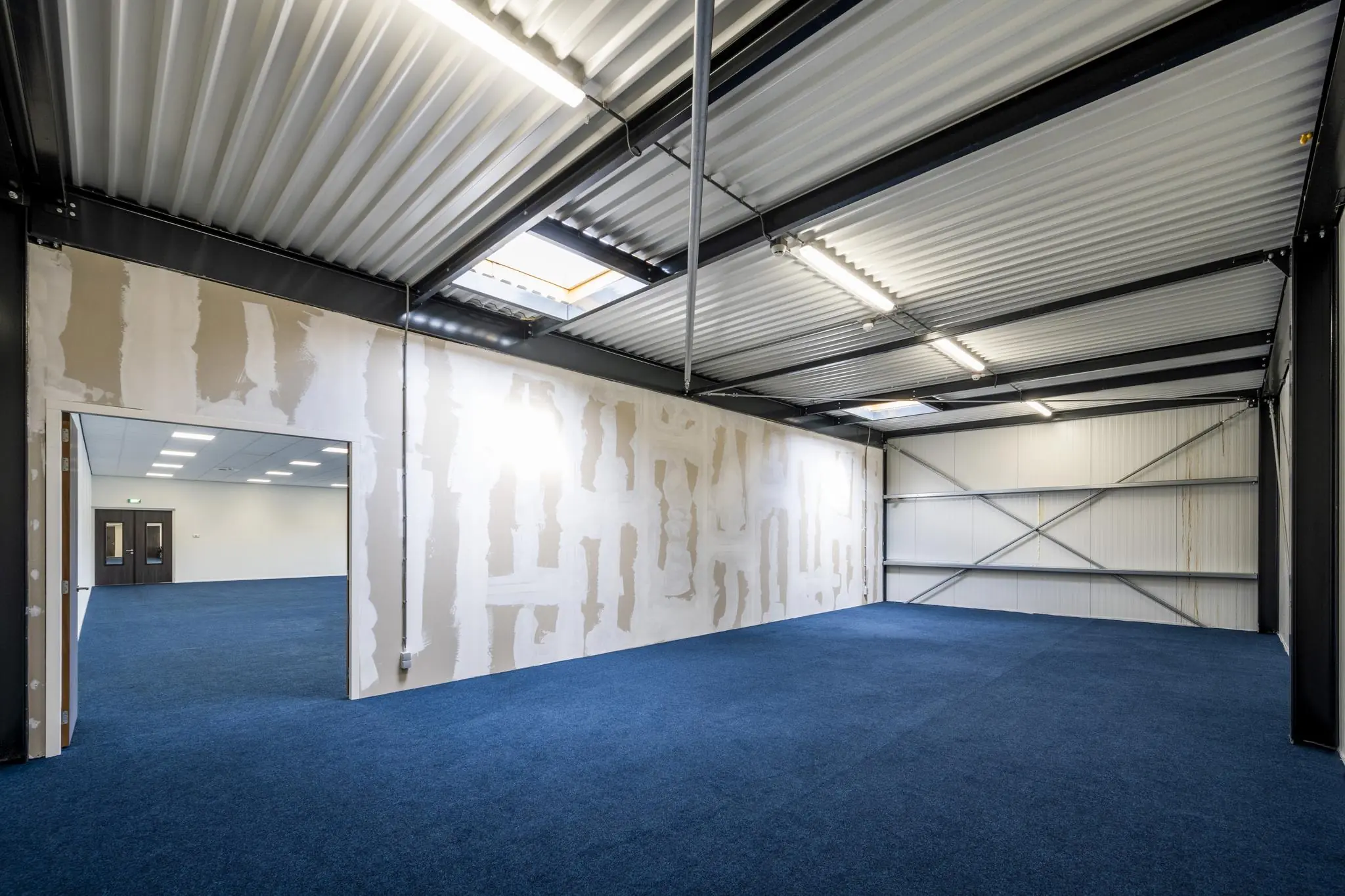 Leeg industrieel kantoor- of bedrijfsruimte aan de Dynamostraat met onafgewerkte tussenwand en blauw tapijt.