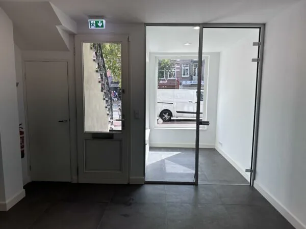 Inkomhal met glazen deur en doorkijk naar de Ceintuurbaan met geparkeerde witte bestelbus.