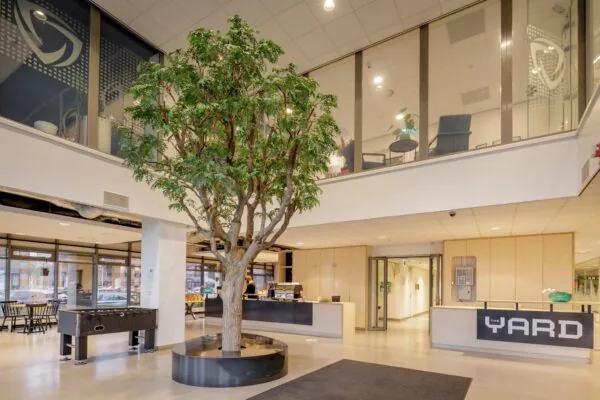 Moderne entree van het gebouw aan de Karspeldreef met een centrale boom, receptiebalie van The Yard en een lounge op de bovenverdieping.