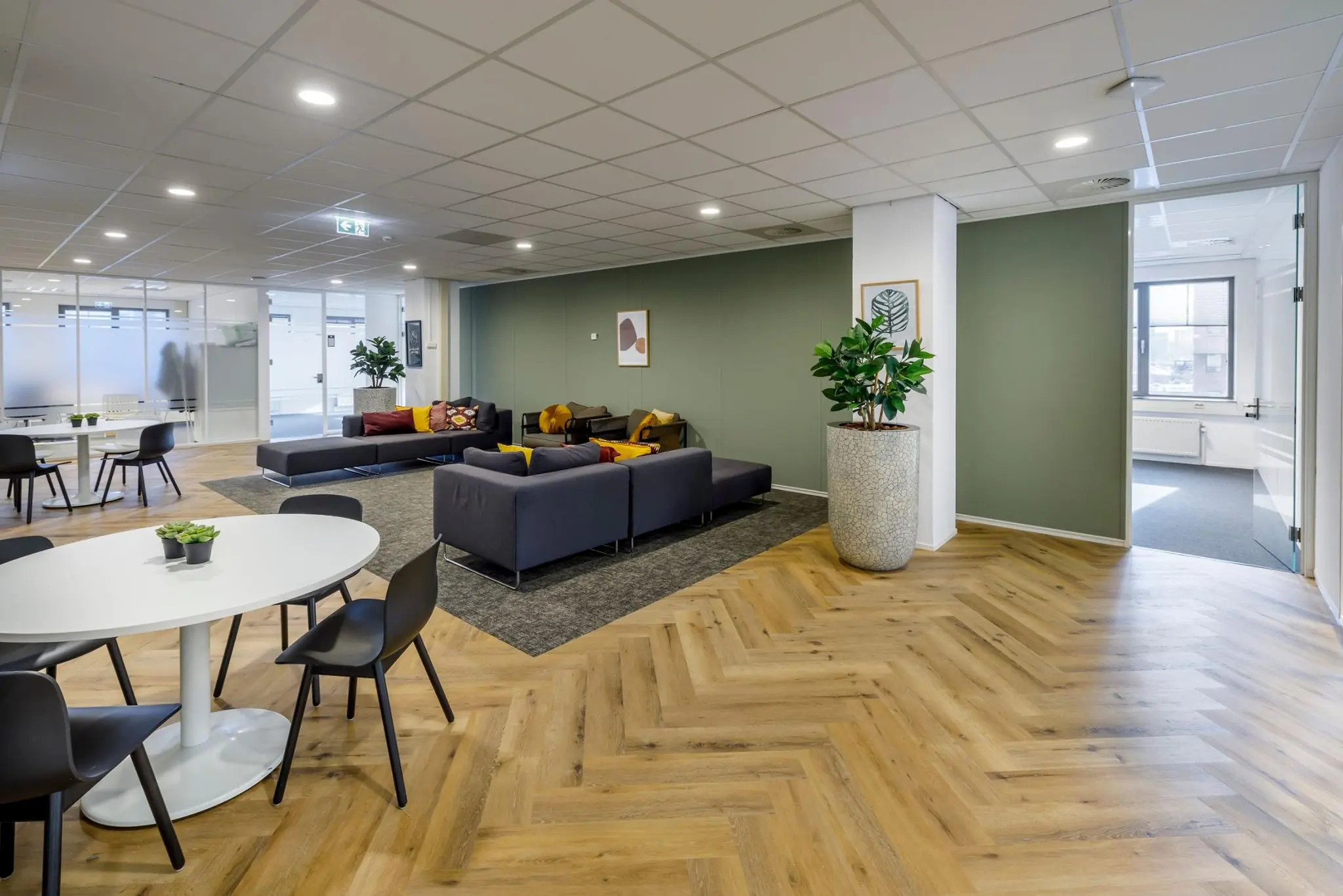 Moderne en open kantoorlounge aan de Karspeldreef met zithoeken, ronde tafels en houten visgraatvloer.