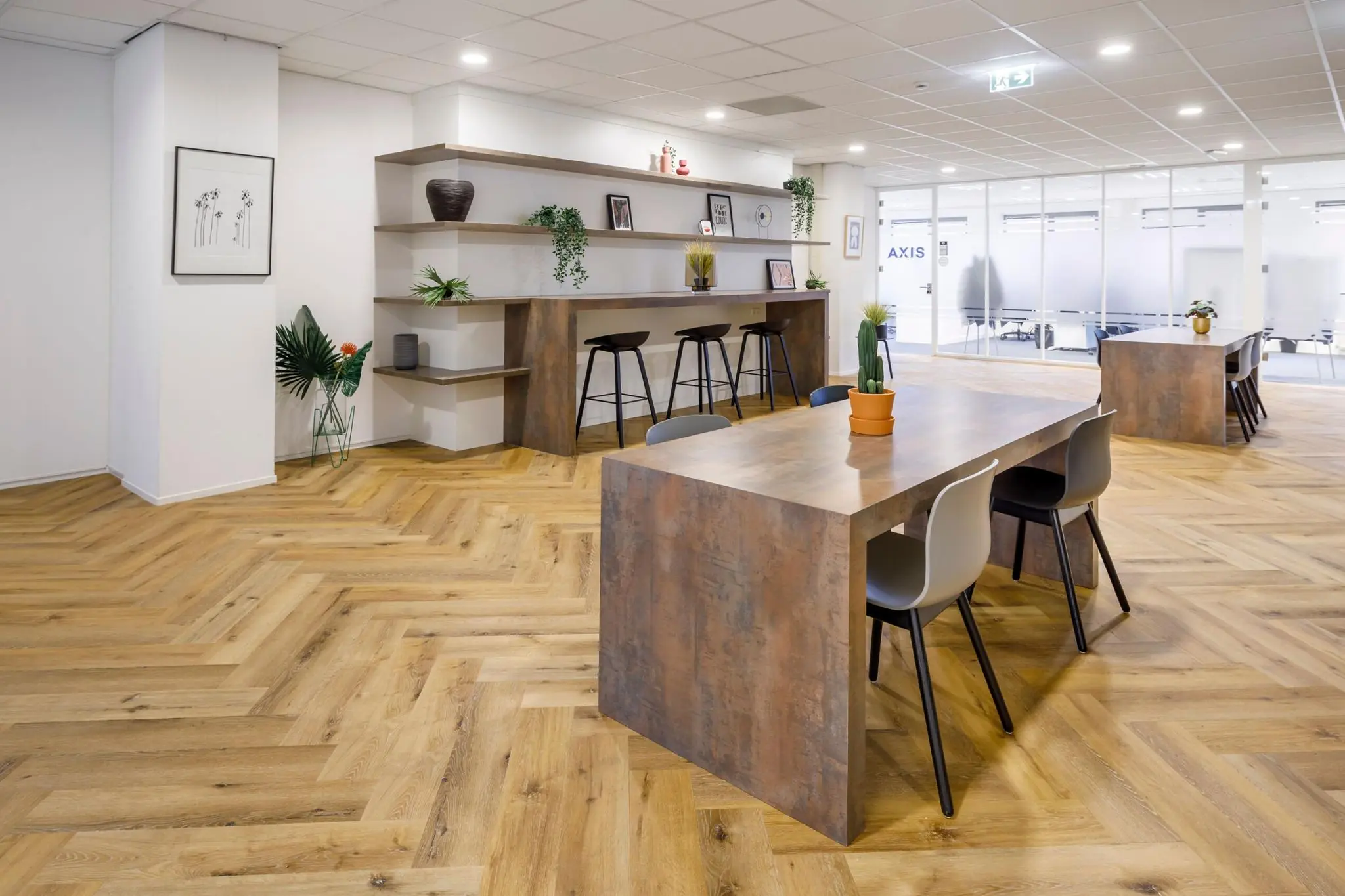 Moderne en open kantoorruimte aan de Karspeldreef met houten visgraatvloer, werktafels en decoratieve planten.